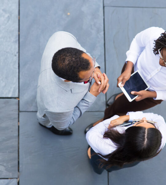 Group of confident workers talking outdoors. Top view of three colleagues meeting on street. Business meeting concept